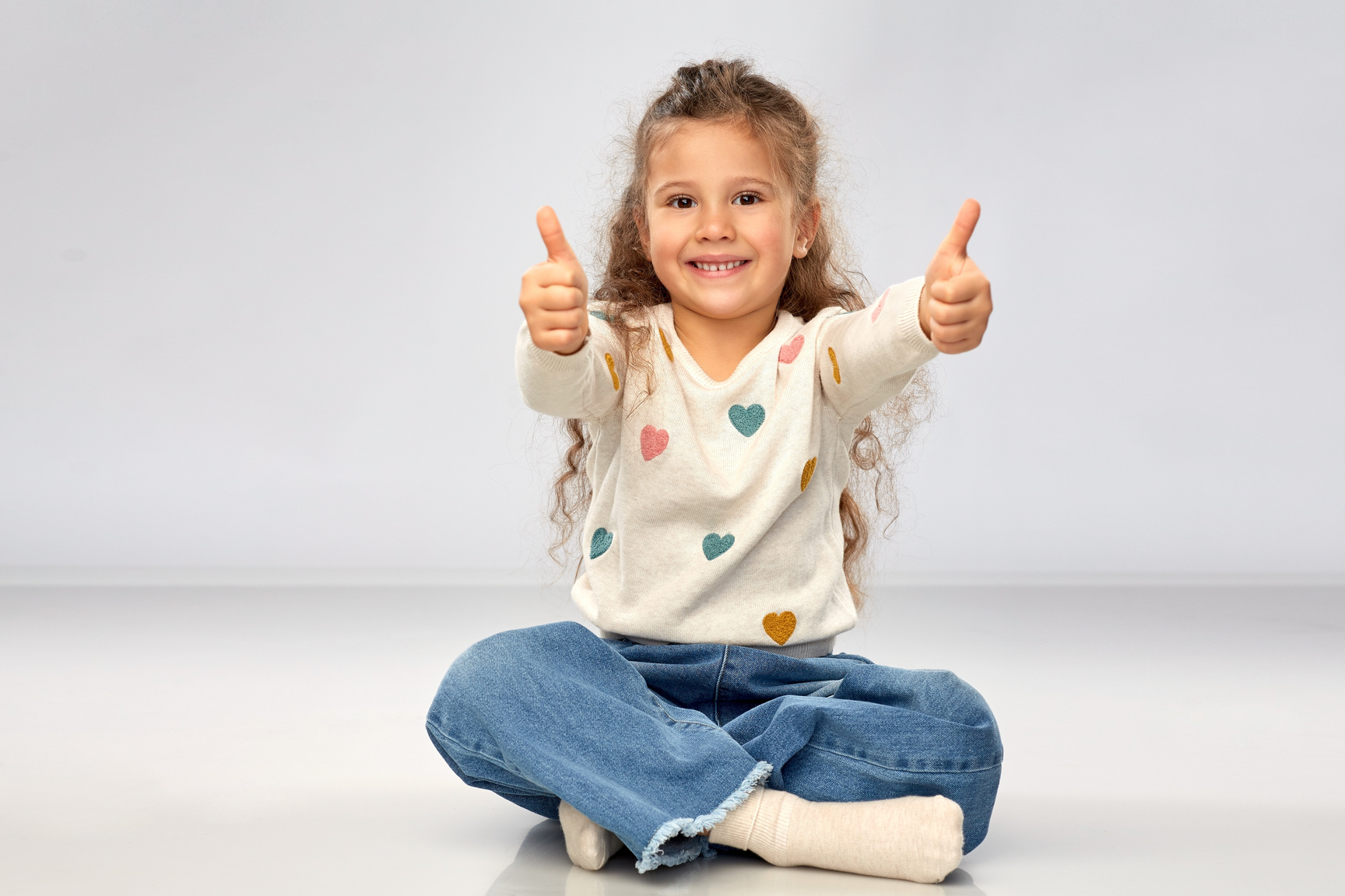 Little Girl Sitting on Floor and Showing Thumbs-up