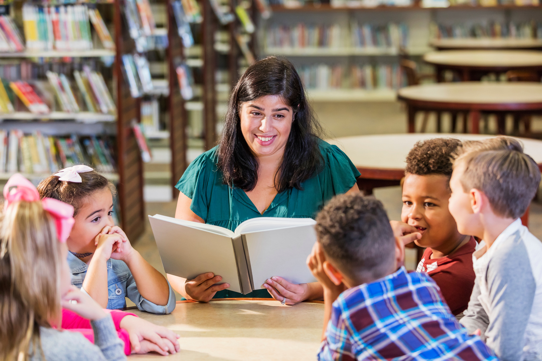 Hispanic teacher reading to children in library