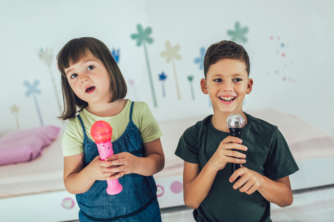 Portrait of a happy children singing karaoke through microphone at home.